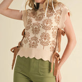 Woman wearing a patterned sleeveless top with brown straps on a beige background
